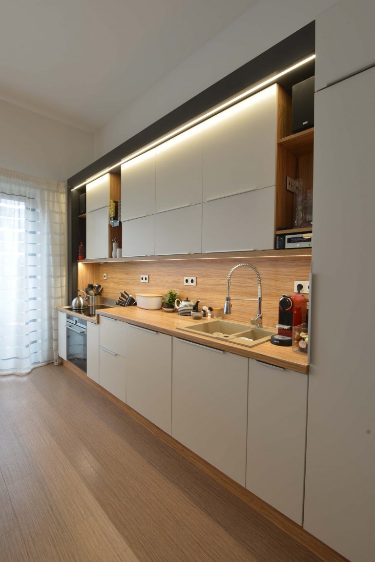 Boční pohled na kuchyň. Kuchyň je osazená v antracitovém lesklém rámu se zabudovaným osvětlením LED a má sníženou varnou zónu. 