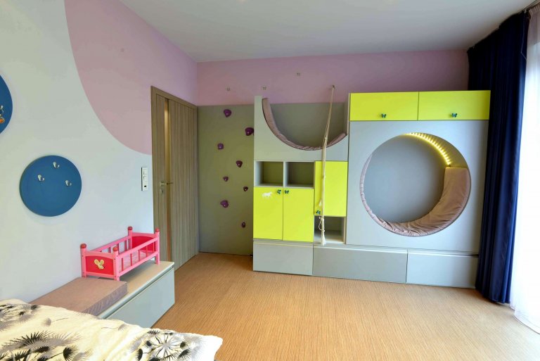 Pohled na nábytkovou sestavu s kulatým a půlkulatým čalouněným sezením a lezeckou stěnou. 