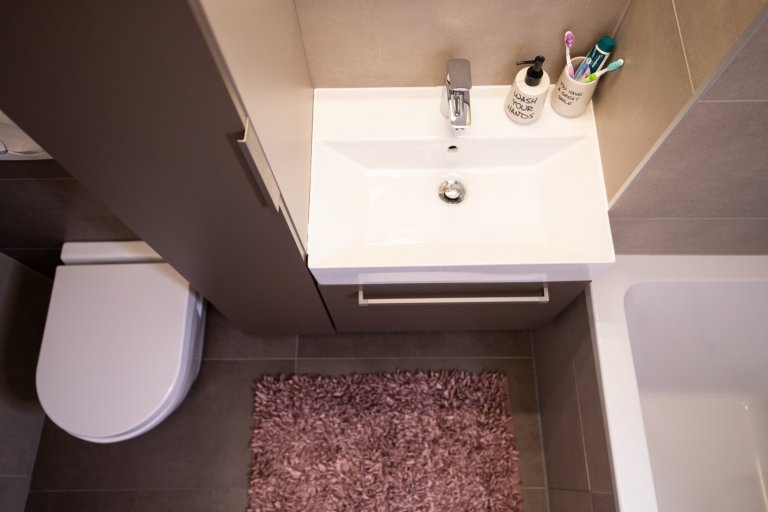 Je dokázáno, že částice při splachování toalety stříkají až jeden a půl metru do okolí. A zajisté nikdo z nás nechce aby se mu něco takového dostalo na kartáček na zuby.  
Proto jsem v této malé koupelně mezi toaletou a umyvadlem navrhla úzkou skříňku, která je nejen vděčný úložný prostor ale i pomyslná stěna mezi splachováním a kartáčkem. 