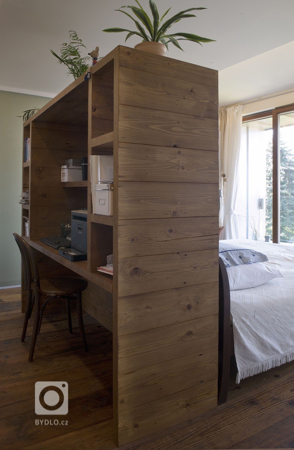 Dělící stěna mezi postelí a pracovnou je současně obostrnnou knihovničkou či nočním stolkem