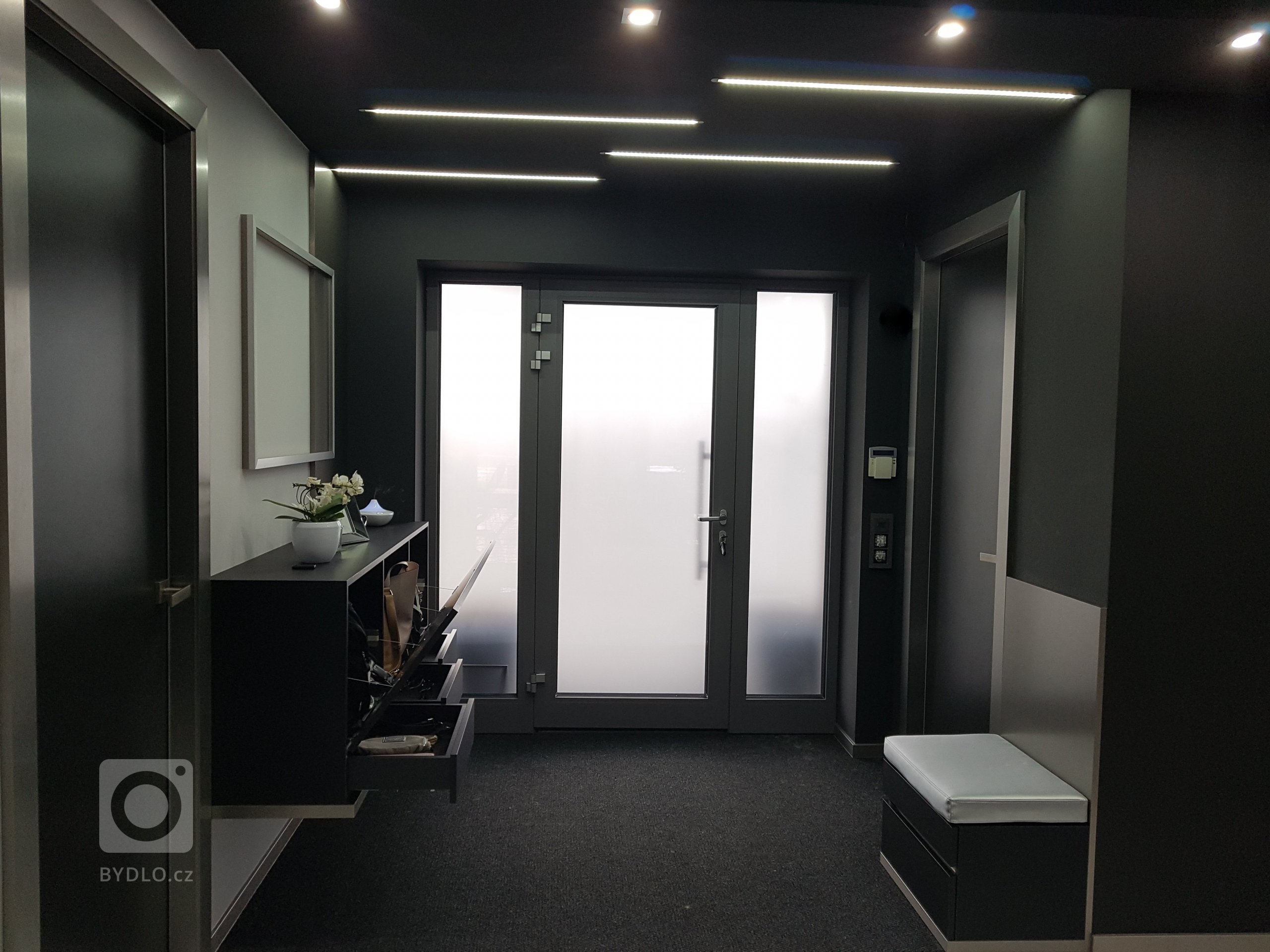 Strop je snížený v černém provedení se zapuštěnými LED pásky. 