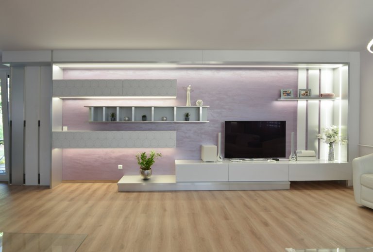 Pohledová stěna pro hlavní sestavu nábytku je uměle orámovaná v kombinaci bílé lesklé a kovolaminátu z kartáčovaného hliníku se zabudovaným osvětlením. Závěsné skřínky jsou z bílé matné s potiskem overface. Regálek je z kovolaminátu. Skřínky jsou výklopné a sklopné, dole jsou hluboké zásuvky. 