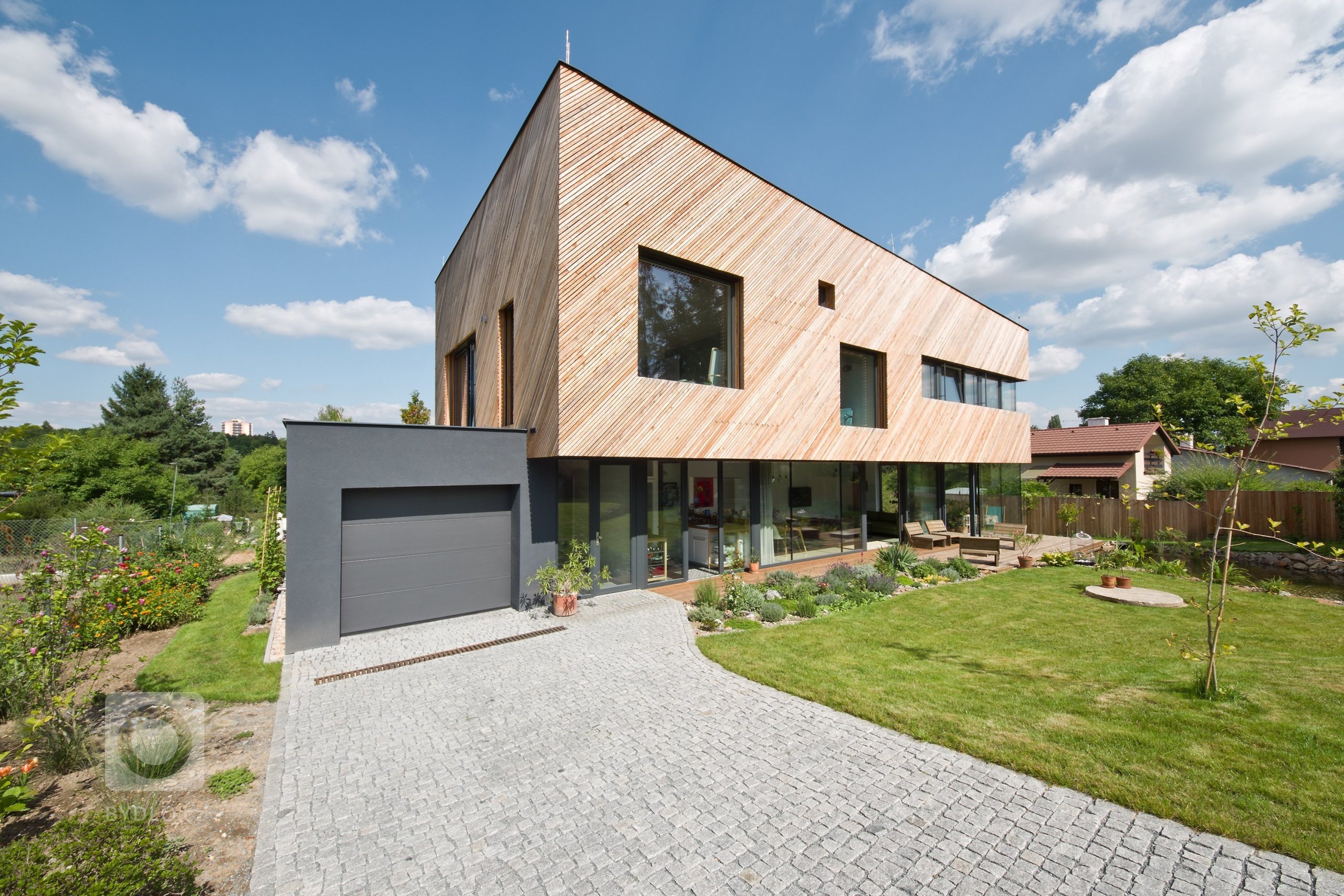 Architektonické řešení navazuje na zahrádkářskou minulost parcely a koncept projektu řadových domů. Protáhlá obdélníková stavba má plně prosklené přízemí, na…