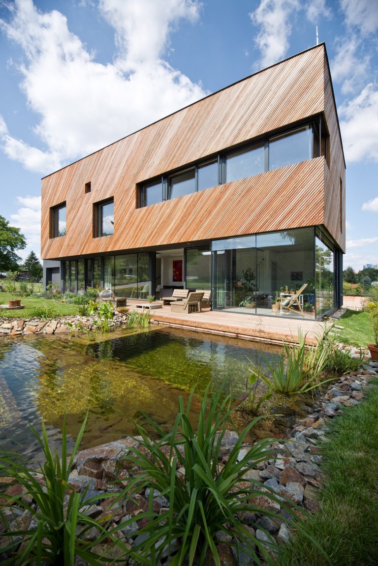Architektonické řešení navazuje na zahrádkářskou minulost parcely a koncept projektu řadových domů. Protáhlá obdélníková stavba má plně prosklené přízemí, na…