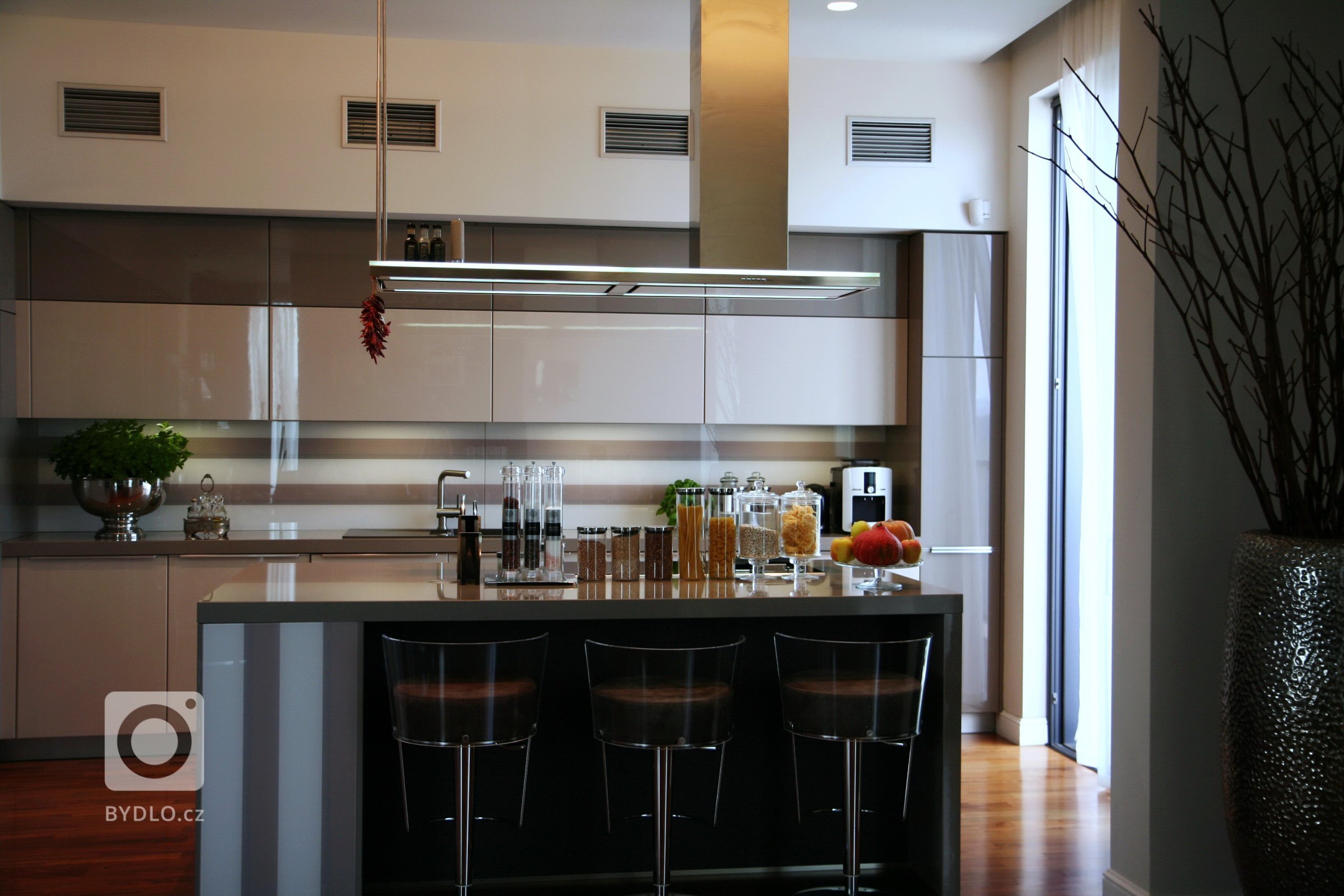 Kuchyně SCHÜLLER GALA -&nbsp;Sestava ve vysokoleském laku, ostrůvek s varným centrem, pracovní desky z technického kamene. Spotřebiče značky De Dietrich a…