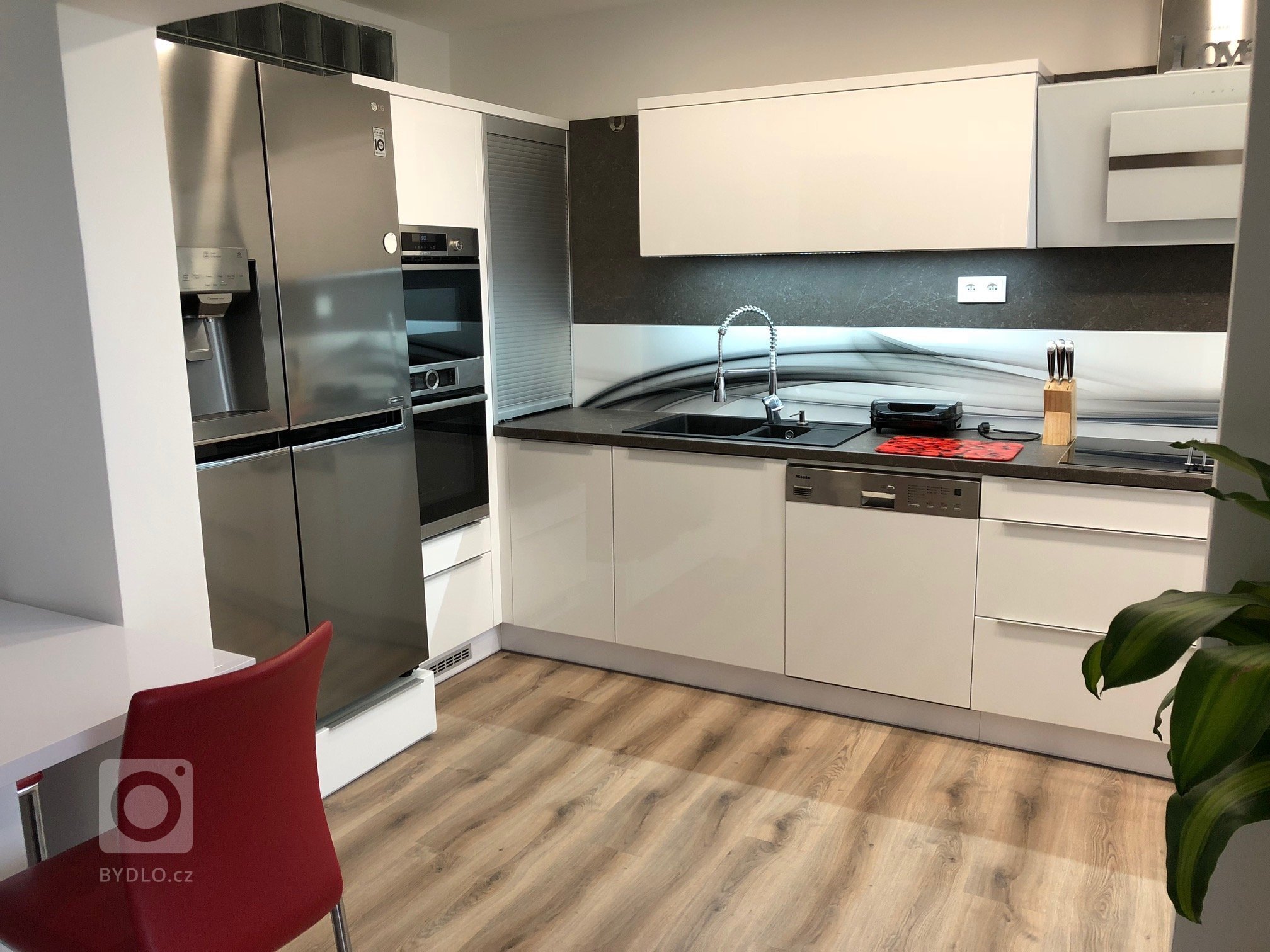 Kuchyňká linka v bílém vysokém lesku s grafosklem, osazená spotřebiči Bosch a doplněná příruční&nbsp;stolovou deskou zabudovanou do skříňkové sestavy…