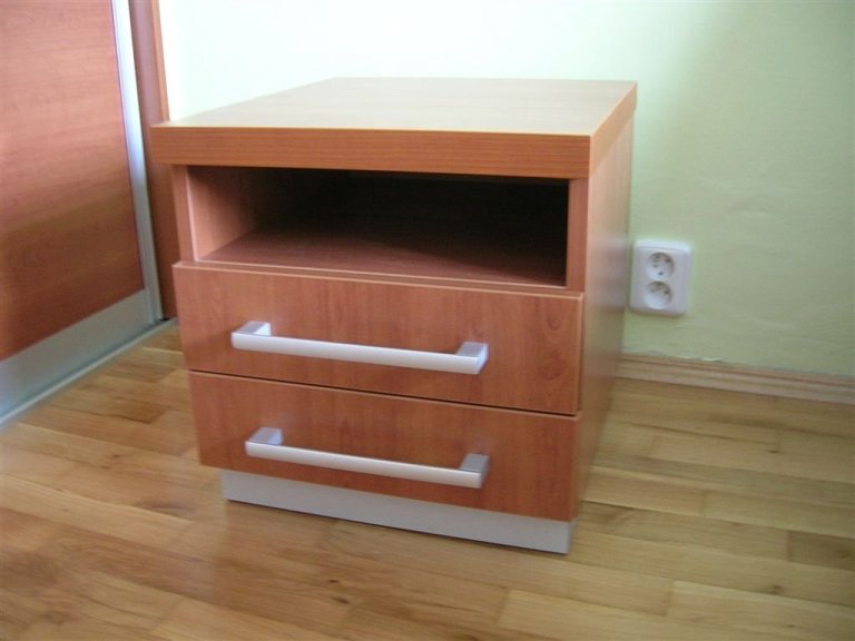 Ložnice s postelí s úložným prostorem, nočními stolky a vestavěnou skříní.
