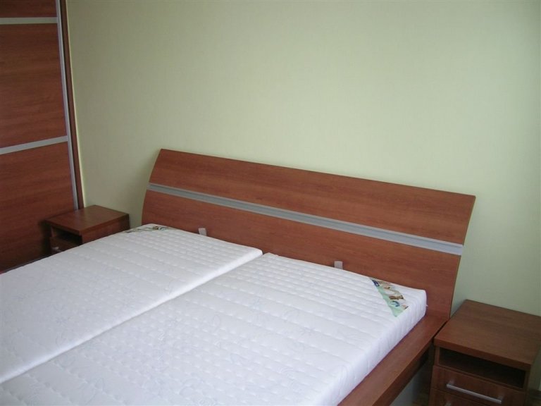Ložnice s postelí s úložným prostorem, nočními stolky a vestavěnou skříní.
