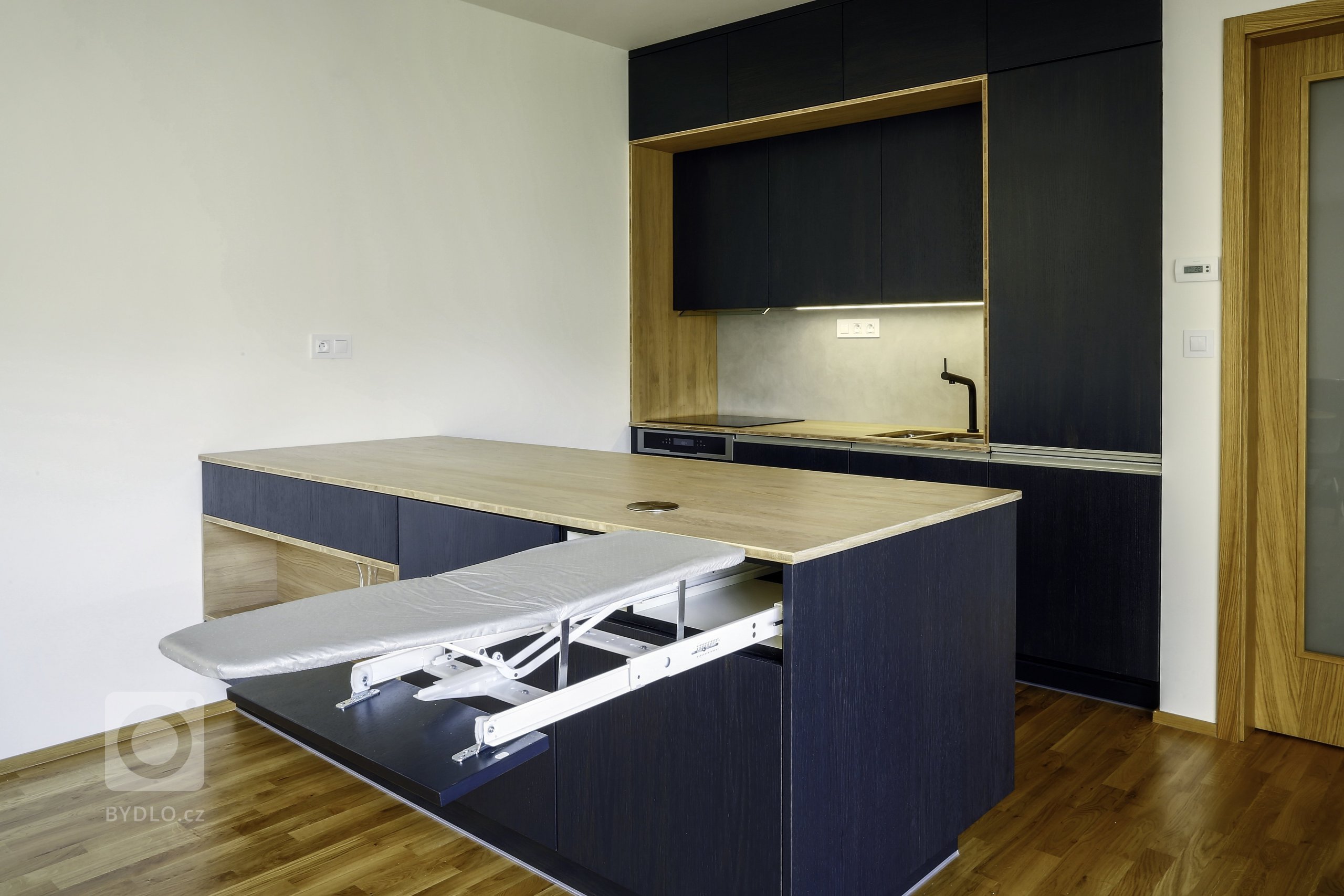 Odvážná kuchyně v novostavbě, kdy je tmavá barva zjemněná dubovou bio deskou a kresba dřeva pod dýhovaným mořeným dvířkem krásně prostupuje a vytváří zajímavý…