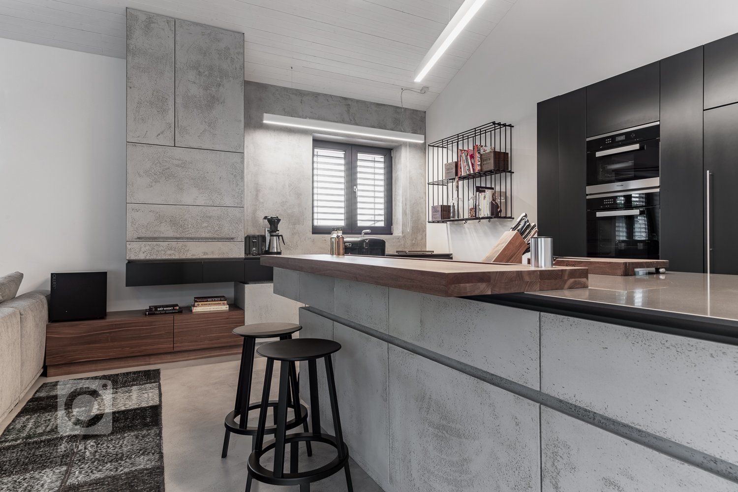 Subtilní pracovní deska z umělého kamene se dostává do kontrastu s masivní barovou deskou z ořechu, s místy k sezení pro dvě osoby.