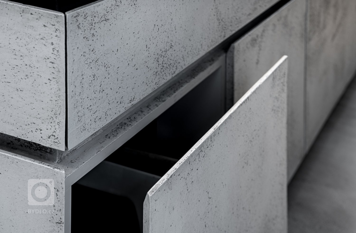 Subtilní pracovní deska je z umělého kamene. Pro zachování čistého designu byla použita kombinace bezúchytkového systému tipon s tichým dojezdem a elektrický systém “servo-drive”. 